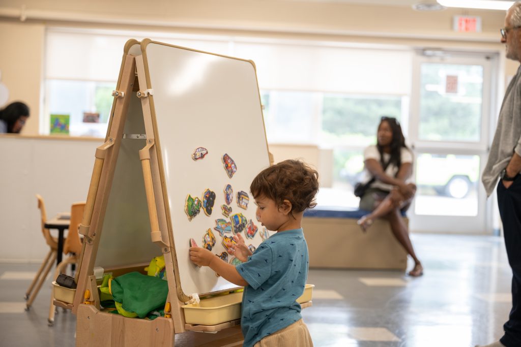 A toddler is busy playing at BrightStart with magnets on an easel.