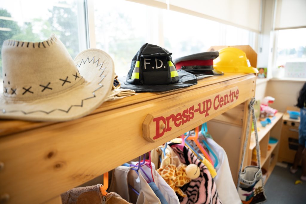 A close up of the dress-up centre at BrightStart for children to have imaginary playtime with western wear, fire fighter clothes, a police hat, construction helmet and more.