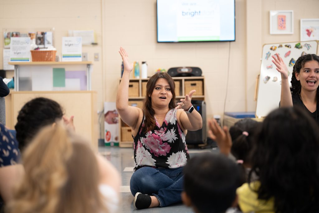 Teachers facing a group of little kids singing and doing actions to songs while having a wonderful time.