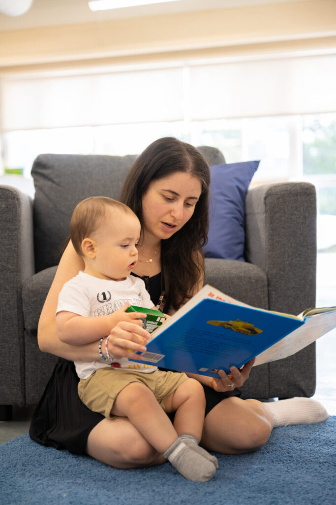 A baby sits on its mothers lap on a mat as a storybook is read