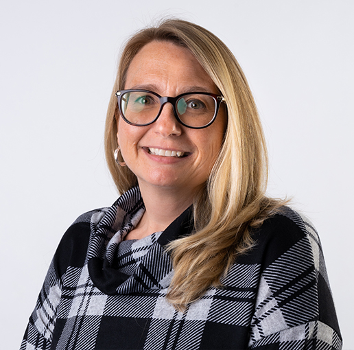 A professional headshot of Lynn Baker, a staff member at BrightStart Caledon Family Centre. She is smiling warmly, wearing glasses and a black and grey plaid-patterned top. Her blonde hair is styled down, and the background is a simple light grey.