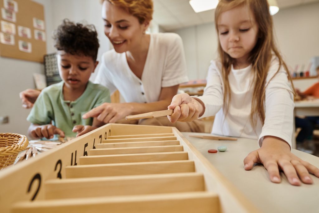 A blurred image of a woman and two children playing with wooden toys together on a table.