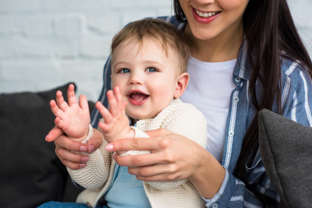 partial view of smiling mother and infant singing and clapping