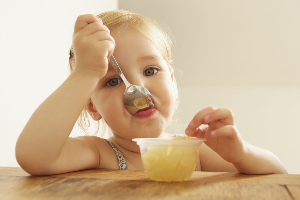 Little girl with blond hair eating apple sauce.