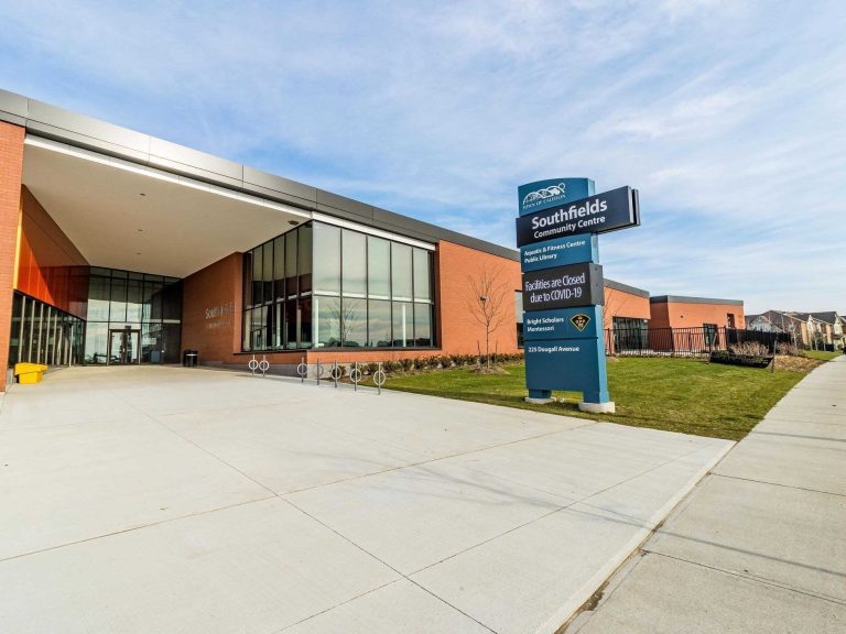 Southfields Community Centre with a modern red-brick exterior, large glass windows, and a sign showing facility closures due to COVID-19. The sign also lists an aquatic and fitness centre, public library, and Bright Scholars Montessori at 225 Dougall Avenue.